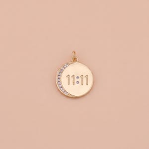 Puede incluir: Colgante dorado con el número "11:11" grabado en el centro. Una forma de media luna, incrustada con pequeños cristales transparentes, enmarca la parte superior izquierda del colgante. El colgante tiene un pequeño lazo en la parte superior para una cadena.