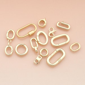 May include: A collection of gold-colored jewelry clasps and connectors in various shapes and sizes. The assortment includes oval, round, and rectangular designs, as well as a figure-eight clasp. The clasps are displayed on a light pink background.