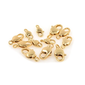 Può includere: Una collezione di chiusure a moschettone dorate, ideali per la creazione di gioielli. Le chiusure sono di varie dimensioni e forme, con una superficie lucida e riflettente. Sono disposte su uno sfondo bianco, evidenziando il loro design.
