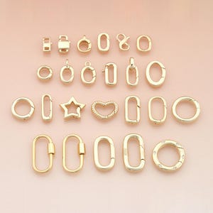 Può includere: Una collezione di chiusure e connettori per gioielli color oro in varie forme, tra cui cerchi, ovali, rettangoli e un design a stella e cuore. Le chiusure sono esposte su una superficie rosa chiaro.