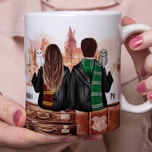 May include: White ceramic mug featuring a colourful illustration of two people in wizard robes standing back to back with owls in their hands. The background depicts a castle and the text "Niki" and "PB".