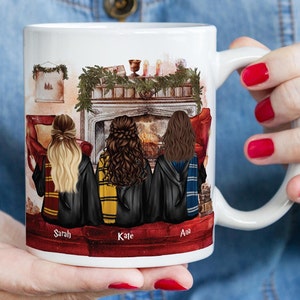 May include: White ceramic mug with a colorful illustration of three women in robes sitting in front of a fireplace. The women are facing away from the viewer and the mug has the names "Sarah", "Kate", and "Ana" written below them.