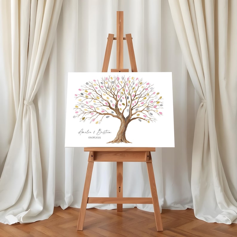 K&ouml;nnte beinhalten: Eine Holzstaffelei zeigt eine wei&szlig;e Leinwand mit einem Aquarellbaum-Design. Der Baum hat farbenfrohe blattf&ouml;rmige Akzente, mit den Namen "Amelia & Bastien" und dem Datum "09.08.2025" darunter. Die Staffelei steht vor wei&szlig;en Vorh&auml;ngen.