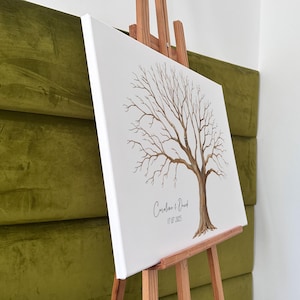 K&ouml;nnte beinhalten: Eine wei&szlig;e Leinwand mit einer braunen Baumillustration, pr&auml;sentiert auf einer h&ouml;lzernen Staffelei. Der Baum hat kahle &Auml;ste und einen dicken Stamm. Die Namen "Caroline & David" und das Datum "17.07.2025" sind darunter geschrieben.