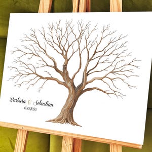 K&ouml;nnte beinhalten: Aquarell-Illustration eines Baumes auf wei&szlig;er Leinwand, pr&auml;sentiert auf einer Holzstaffelei. Der Baum hat einen braunen Stamm und &Auml;ste, mit den Namen "Barbara & Sebastian" und dem Datum "15.10.2025" darunter. Der Hintergrund ist ein sanftes Gr&uuml;n.