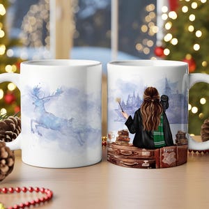 Könnte beinhalten: Zwei weiße Keramikbecher. Ein Becher zeigt ein Aquarellbild eines blauen Hirsches, der durch eine verschneite Szene springt. Der andere Becher zeigt eine Person mit Zauberstab, Eule und Schloss. Die Becher stehen auf einer Holzoberfläche.