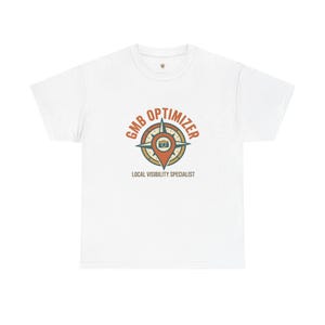 May include: A white short-sleeve t-shirt featuring a central graphic of a compass rose combined with a map location pin and a small camera icon. The text GMB OPTIMIZER is arched above the graphic, with LOCAL VISIBILITY SPECIALIST printed below.