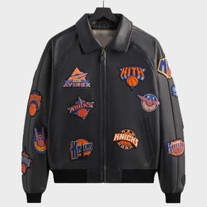 May include: A black leather jacket featuring a full-length front zipper, a classic collar, and ribbed cuffs and hem. The jacket is decorated with various embroidered patches, including the text "KITH," "AVIREX," and "KNICKS" with basketball graphics.