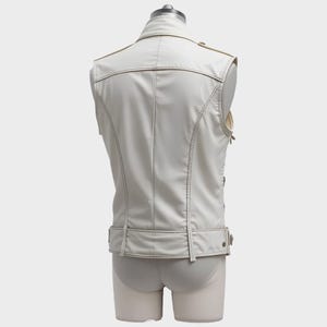 May include: A cream-colored, sleeveless vest with a classic biker jacket design. Features include a notched collar, shoulder epaulets, and a belt detail at the waist. The vest has visible stitching and a smooth, matte finish. The vest is displayed on a mannequin.