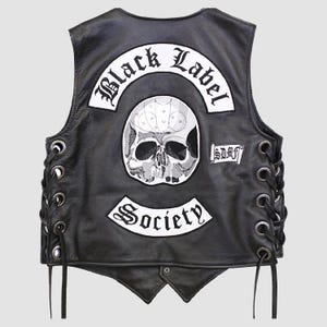 Peut inclure: Gilet en cuir noir avec un motif de crâne et les mots "Black Label Society" et "Society" en blanc. Le gilet a un laçage latéral et un style motard classique.