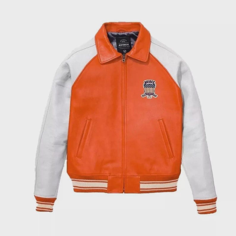 May include: Orange and white leather jacket with a zip-up front, a collar, and a patch on the chest. The sleeves are white, and the body is orange. The cuffs and waistband have white and orange stripes. The jacket has a classic varsity style.