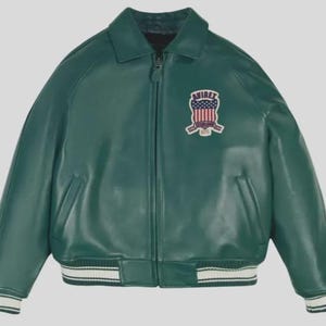 Puede incluir: Chaqueta de cuero verde con cremallera, cuello y pu&ntilde;os y dobladillo acanalados. La chaqueta presenta un parche en el pecho con el texto "AVIREX" y un dise&ntilde;o que incorpora la bandera estadounidense. Dos bolsillos delanteros.