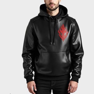 Puede incluir: Sudadera con capucha negra con un diseño de llama roja en el pecho. La sudadera tiene un bolsillo de canguro y una capucha con cordón. El material parece ser cuero sintético o un tejido similar al cuero.