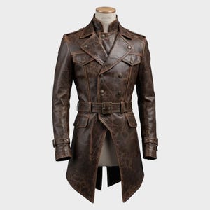 May include: A brown leather trench coat with a double-breasted design. The coat features a belt, multiple pockets, and button details. The distressed leather has a vintage look. The coat is displayed on a mannequin.