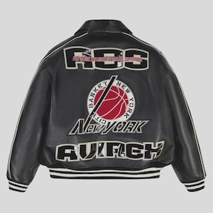 Puede incluir: Chaqueta de cuero negra con ribete blanco y el texto "RSC AVIREX BASKETBALL SPORTS" en los hombros. Un gráfico de baloncesto con "New York" está centrado en la espalda, con "AVIREX" debajo.