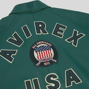Puede incluir: Chaqueta verde oscuro con la palabra "AVIREX" en letras blancas con contorno azul oscuro. Un parche circular con la bandera americana y las palabras "ALL AMERICANS ESTABLISHED NY 1975" est&aacute; centrado debajo.