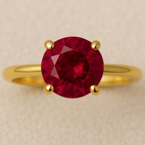 May include: A gold ring with a large, round, faceted ruby gemstone. The ruby is a deep red colour and is held by four gold prongs. The ring's band is a simple, polished gold.