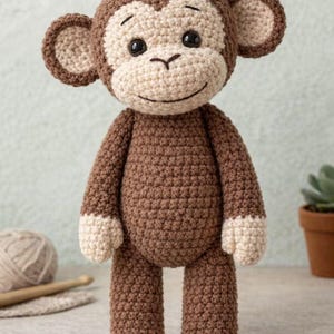 Puede incluir: Un muñeco de mono de ganchillo hecho a mano en tonos marrón y crema. El mono tiene una cara sonriente, orejas grandes y está de pie. El muñeco está hecho con una puntada texturizada, lo que le da un aspecto suave. Un juguete encantador y tierno.