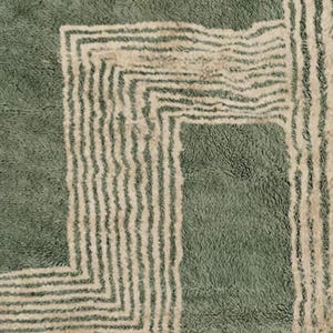 Pu&ograve; includere: Primo piano di un tappeto verde e beige con un design geometrico. Il tappeto presenta un pelo morbido e strutturato con un motivo ripetuto di linee beige su sfondo verde. Il design include un bordo quadrato e strisce verticali.