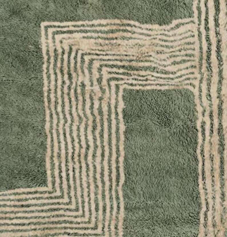 Pu&ograve; includere: Primo piano di un tappeto verde e beige con un design geometrico. Il tappeto presenta un pelo morbido e strutturato con un motivo ripetuto di linee beige su sfondo verde. Il design include un bordo quadrato e strisce verticali.