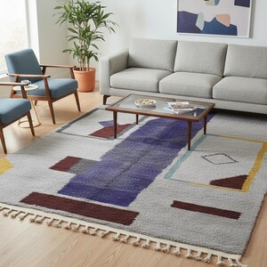 以下が含まれることがあります： グレー、紫、茶色、黄色、ターコイズブルーの色合いの幾何学模様が特徴的なモダンなラグ。 長方形のラグは、下端にフリンジが付いています。 家具のあるリビングルームに配置されています。
