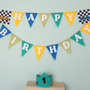 May include: A colorful birthday banner with pennants spelling "HAPPY BIRTHDAY" and car-themed accents. Includes a teal crown with the number "1" and car designs, perfect for a first birthday celebration.
