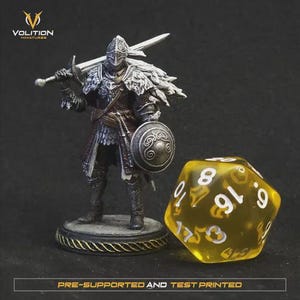 Puede incluir: Una figura en miniatura de un caballero con armadura plateada, sosteniendo una espada y un escudo, junto a un dado grande amarillo de veinte caras. La base de la figura es dorada y negra. El texto "PRE-SUPPORTED AND TEST PRINTED" está en la parte inferior.