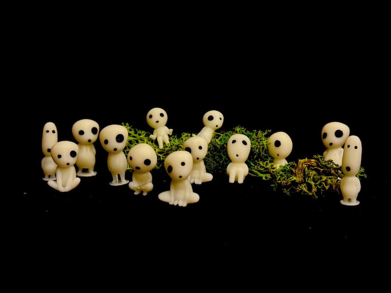 May include: A collection of small, off-white figurines with large, black eyes and simple features. The figures are arranged on a bed of green moss against a black background. Some are standing, others are seated.