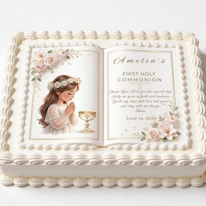 May include: A square cake with white icing and a decorative border. The cake is topped with an edible image of a girl in a white dress, a floral crown, and a chalice. Text on the image reads "Amelia's First Holy Communion" and a prayer. The date June 14, 2026 is also included.