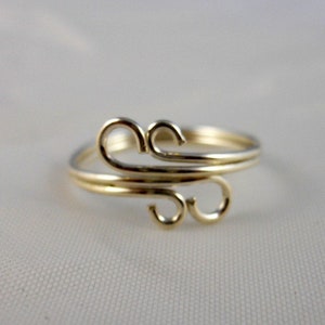 Puede incluir: Un anillo dorado con un diseño delicado y en espiral. El anillo está hecho de alambre fino y tiene un estilo simple y elegante.