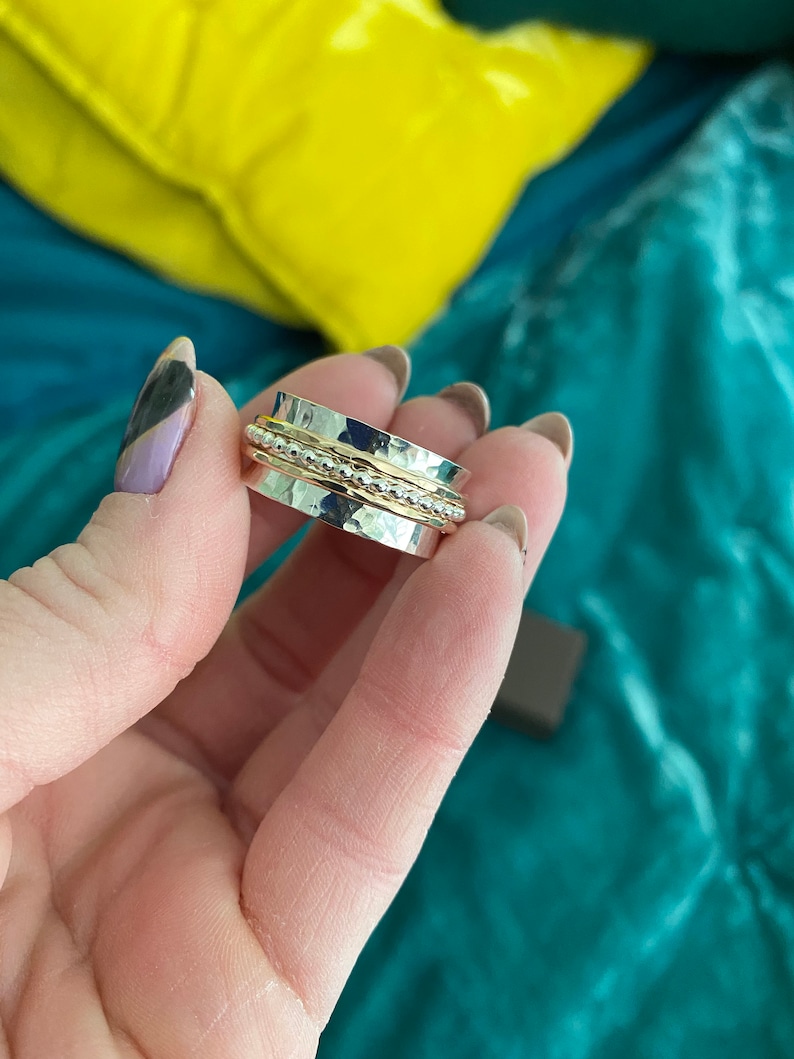 May include: A silver and gold spinning ring with a hammered texture. The ring has three bands with a beaded detail.