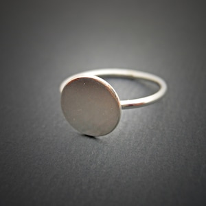 May include: A silver ring with a large, round, flat top.