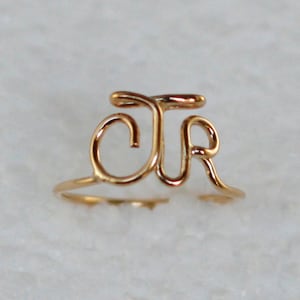 Puede incluir: Anillo dorado con las letras "JR" entrelazadas en un delicado diseño de alambre.