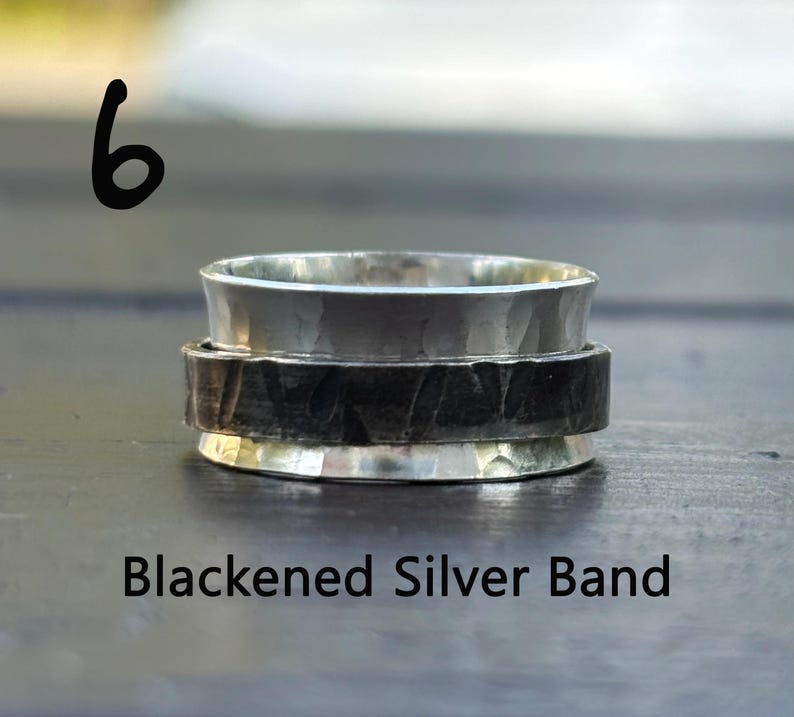 May include: A silver spinning ring with a blackened silver band. The ring is made of two pieces, one silver and one blackened silver.