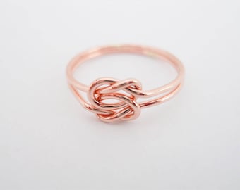 May include: A rose gold knot ring with a simple design. The ring is made of two intertwined bands of metal.