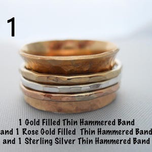 May include: Three thin hammered metal bands stacked on top of each other. The top band is gold filled, the middle band is rose gold filled, and the bottom band is sterling silver.