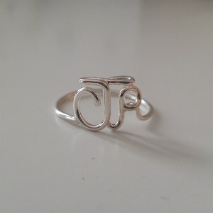 Könnte beinhalten: Ein silberner Ring mit den Buchstaben "JP" ineinander verschlungen.