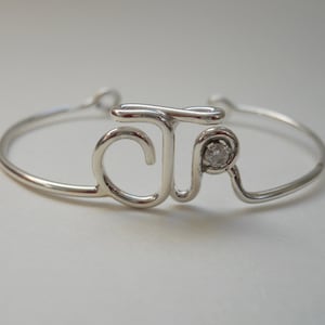 May include: A silver bracelet with the letters "JR" intertwined and a small clear rhinestone in the center.