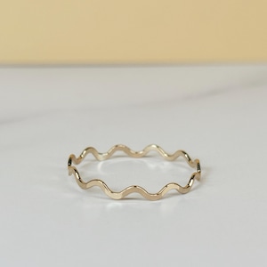 Puede incluir: Un anillo fino de oro pulido que presenta un diseño ondulado o serpentino continuo. La banda tiene un acabado metálico liso y reflectante, con un patrón curvo consistente y repetitivo que rodea toda la circunferencia del anillo.