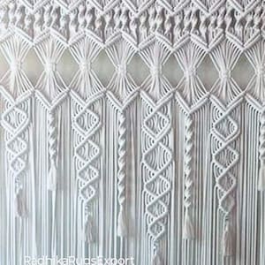 Könnte beinhalten: Ein weißer Makramee-Wandbehang mit geometrischem Design. Das Stück weist Rauten- und Zickzackmuster auf, mit langen Quasten, die von unten hängen. Das Makramee besteht aus dicken, gewebten Baumwollschnüren, die einen strukturierten, böhmischen Look erzeugen.