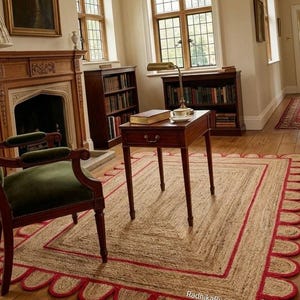 Puede incluir: Una alfombra rectangular de yute con un borde rojo festoneado y un borde interior rojo. La alfombra está en una habitación con chimenea, estanterías y una pequeña mesa de madera. La habitación tiene pisos de madera y ventanas grandes.