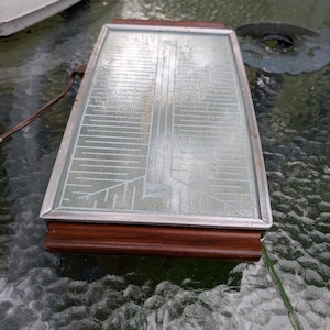 May include: A rectangular electric warming tray featuring a glass surface with a white etched circuit-like pattern and the Salton brand name. The tray is framed in silver-toned metal and includes dark brown wooden handles on both ends.