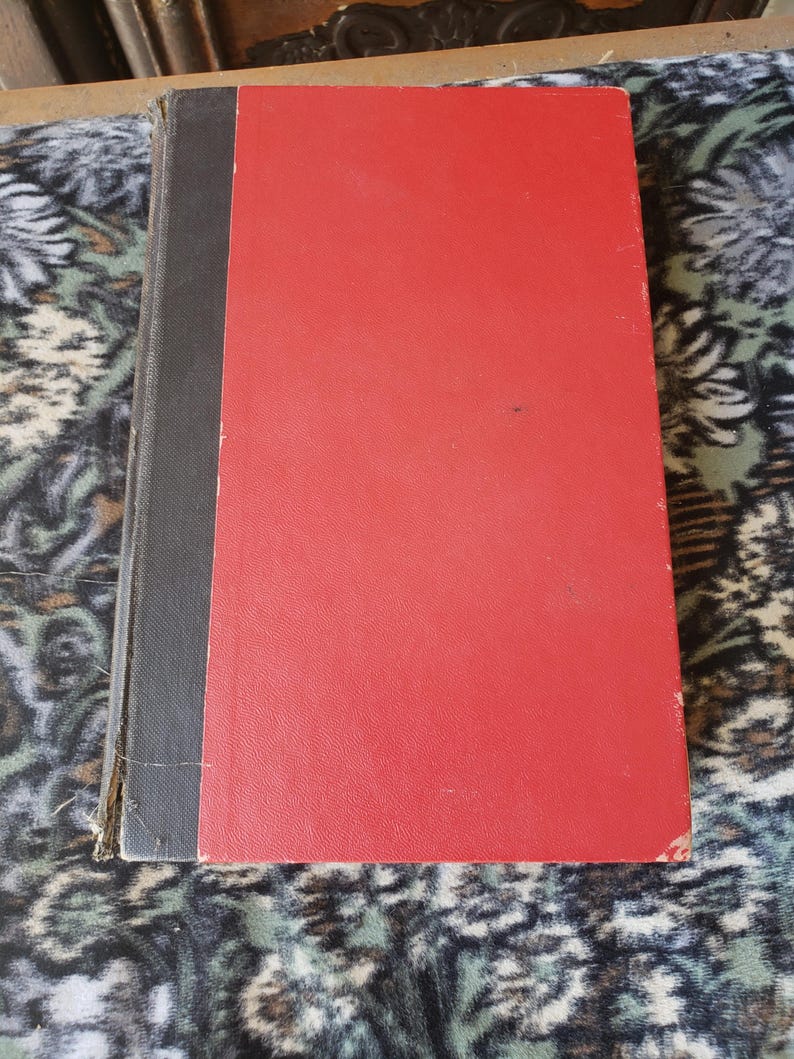 May include: A hardback book featuring a bright red front cover and a dark grey spine. The book has a rectangular shape with visible wear along the edges of the spine and corners of the cover, showing signs of age and use on the binding material.