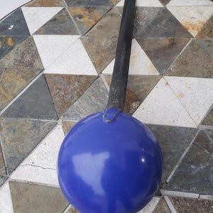 May include: A blue, spherical object with a long, black handle. The object appears to be a vintage or antique kitchen tool, possibly a ladle or a similar utensil. The handle is attached to the sphere with a metal bracket.