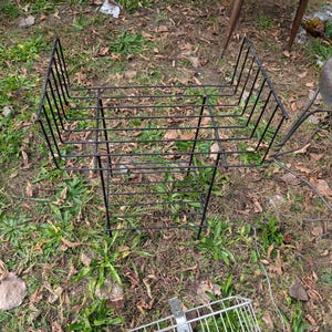 May include: A black metal wire rack with a rectangular frame and a tiered design, featuring a deep upper basket section and a lower shelf, constructed from thin metal rods arranged in a grid pattern for storage or organization.