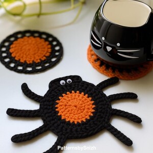 May include: A black and orange crocheted spider coaster with googly eyes, a round black and orange crocheted coaster, and a black cat-shaped ceramic mug resting on an orange crocheted coaster. The text PatternsbySnizh is visible at the bottom.