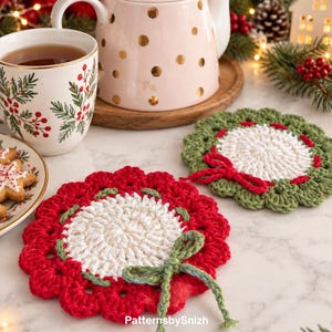 May include: Two round crochet coasters featuring a central white circle surrounded by a scalloped border. One coaster has a red border with a green yarn bow, while the other has a green border with a red yarn bow. Text reads PatternsbySnizh.