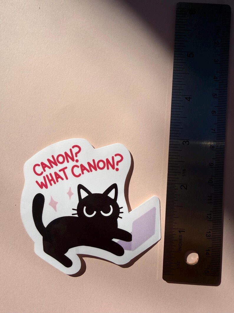 May include: A sticker featuring a black cat with the text "CANON? WHAT CANON?" in red. The cat is drawn with a laptop. The sticker is approximately 3 inches in length.