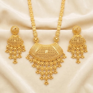 Puede incluir: Un conjunto de joyería en oro que consta de un collar largo y dos pendientes a juego. El collar presenta un colgante grande, curvo y texturizado con dijes circulares colgantes. Los pendientes reflejan el diseño del colgante con patrones.