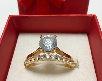 May include: A gold engagement ring with a large, clear central stone and smaller stones along the band, presented in a red gift box with a bow.